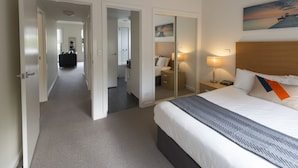 A hotel room with a large bed, a bedside table with a lamp, a mirror, and a painting on the wall. - Quest Frankston (Frankston)