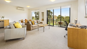 A spacious living area with a sofa, coffee table, and a desk with a laptop. - Quest Frankston (Frankston)