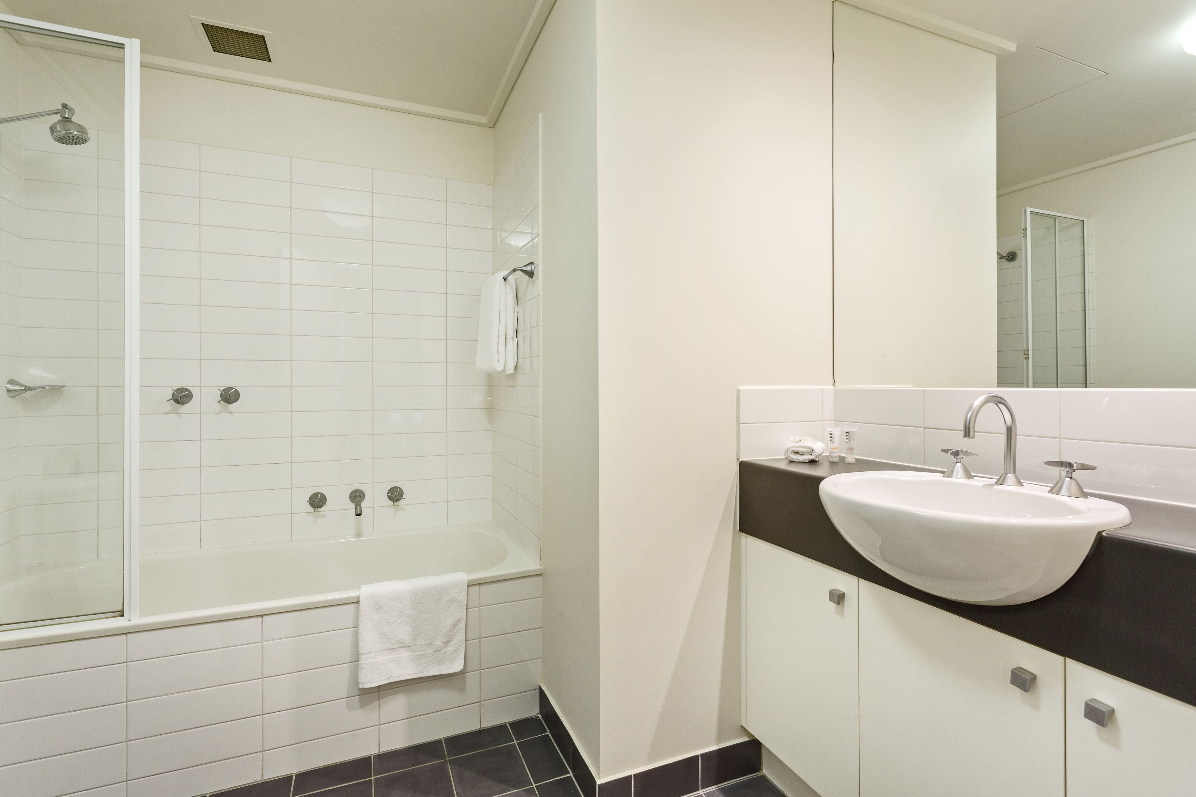 Un baño moderno con ducha acristalada, una bañera blanca y un lavamanos con encimera negra.