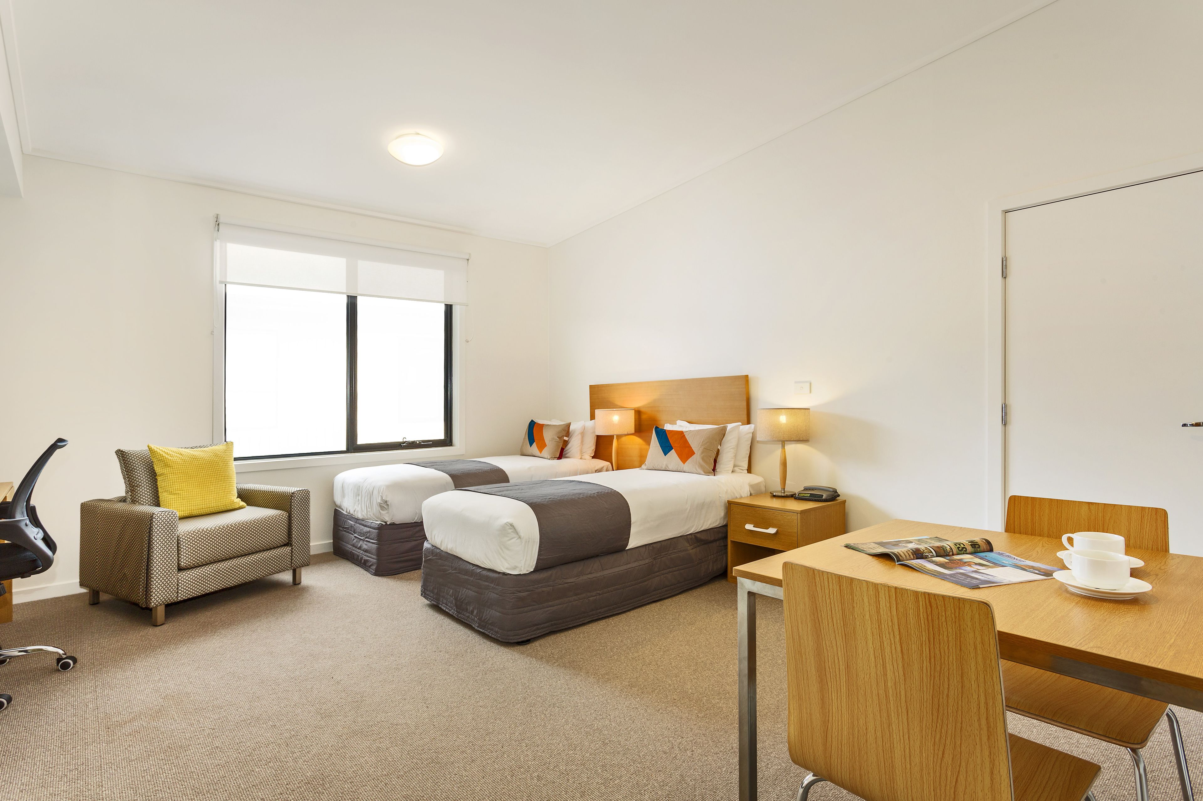 A hotel room with two beds, a desk, a chair, a sofa, and a window.