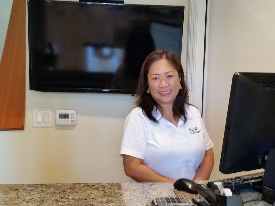 A person standing at a reception desk with a television mounted on the wall above, a thermostat, and a computer monitor to the right.