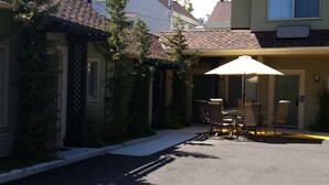 A covered outdoor seating area with a table and chairs, a wheelchair-accessible entrance, and a building with a tiled roof and greenery. - Marin Lodge (San Rafael)