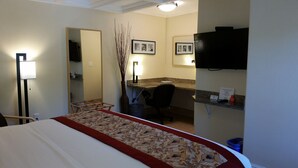 A hotel room with a bed, a desk, a chair, a TV, and a mirror.