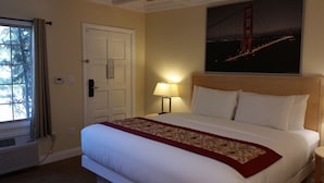 A hotel room with a bed, a nightstand, a lamp, a door, and a window with curtains. - Marin Lodge (San Rafael)
