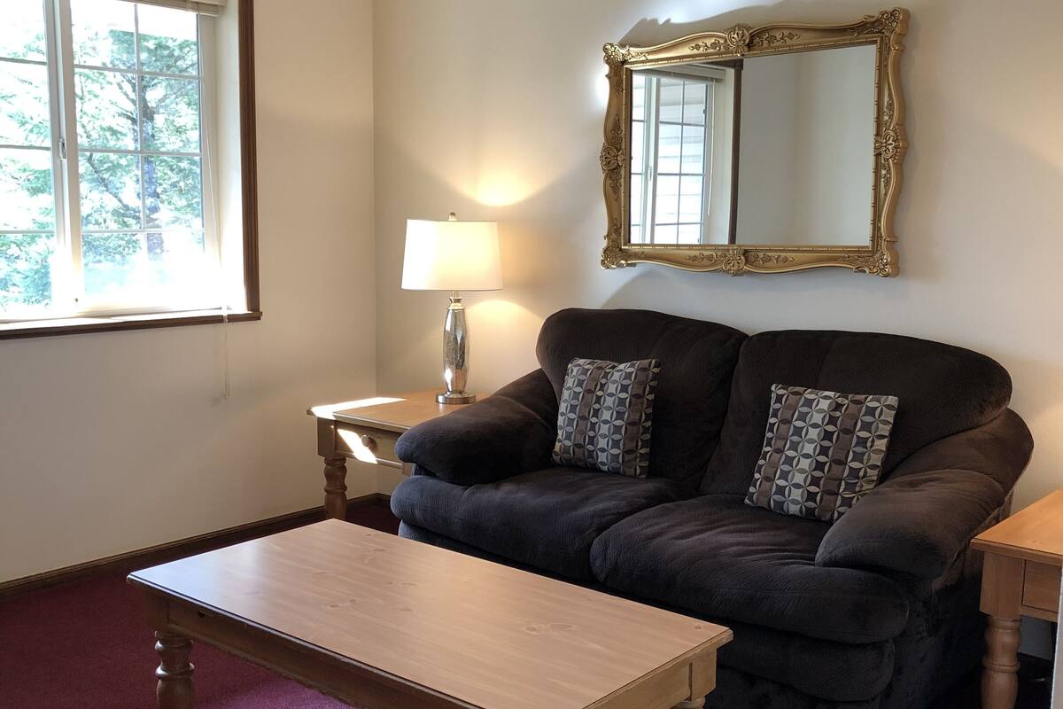 A living room with a dark brown sofa, a wooden coffee table, a lamp, and a large mirror on the wall.