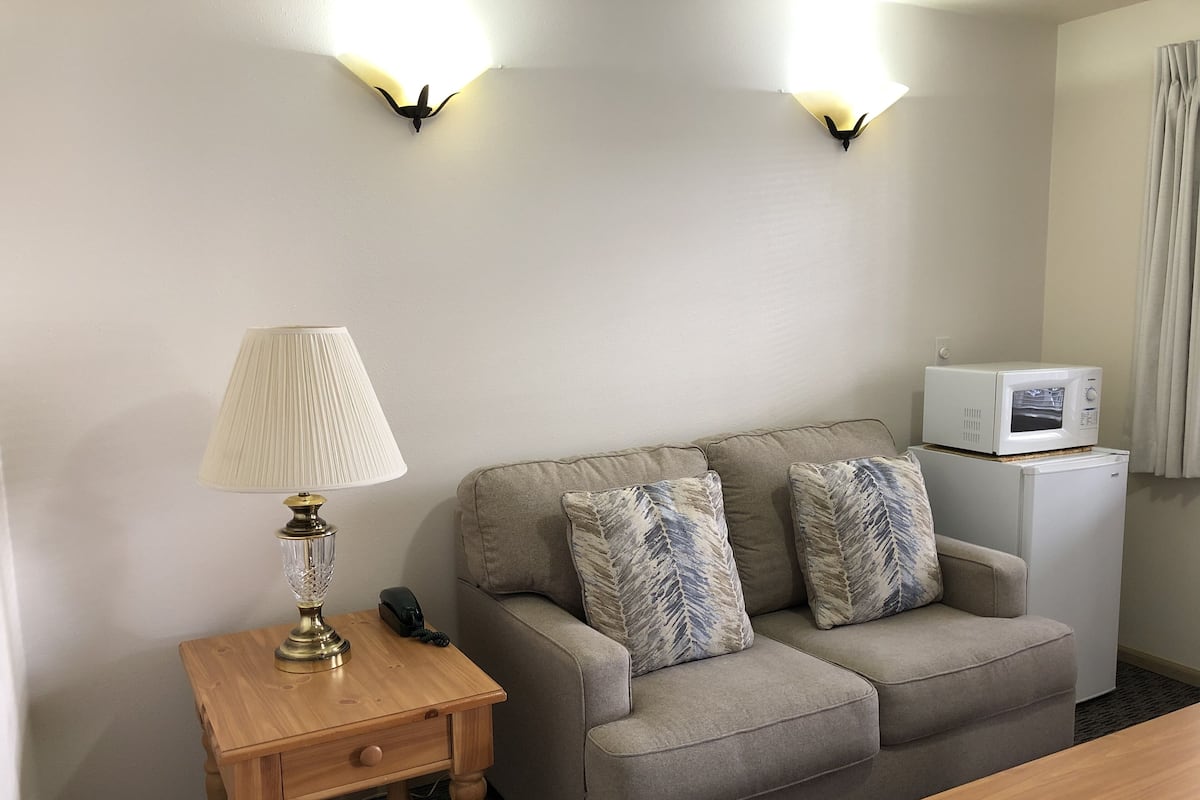 A room with a sofa, a small table with a lamp, a microwave, and a telephone.