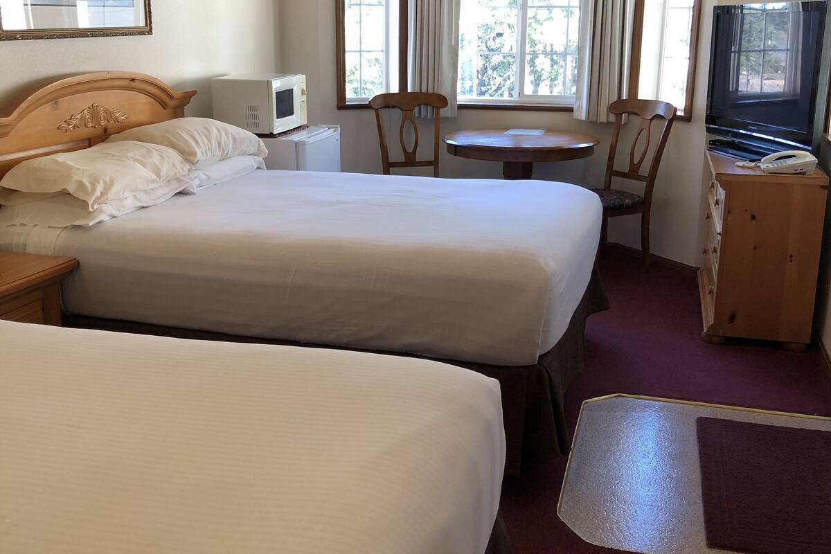 A hotel room with two beds, a desk, a television, and a window with curtains.
