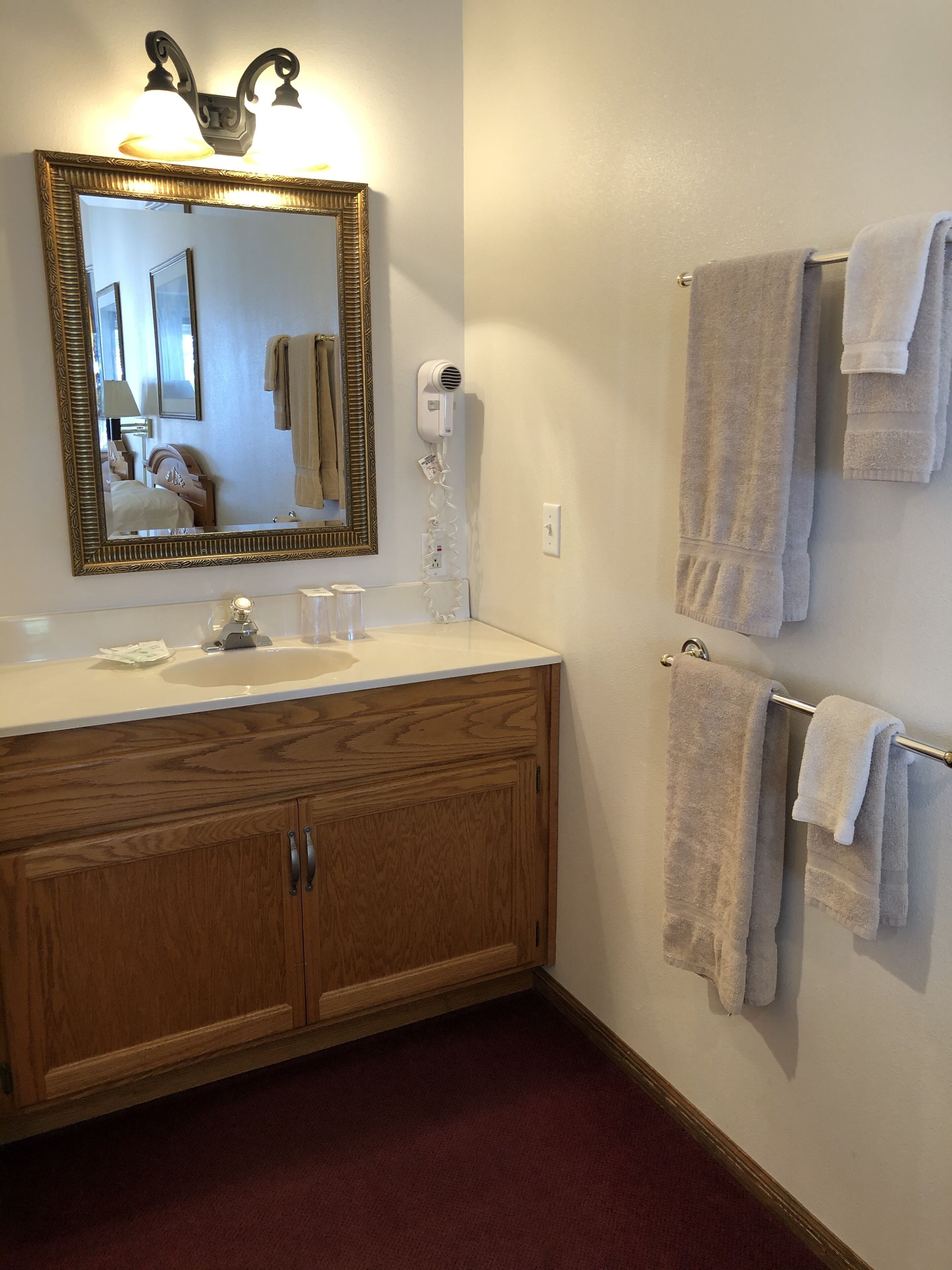 A bathroom with a wooden vanity, a large mirror, and a towel rack with multiple towels.