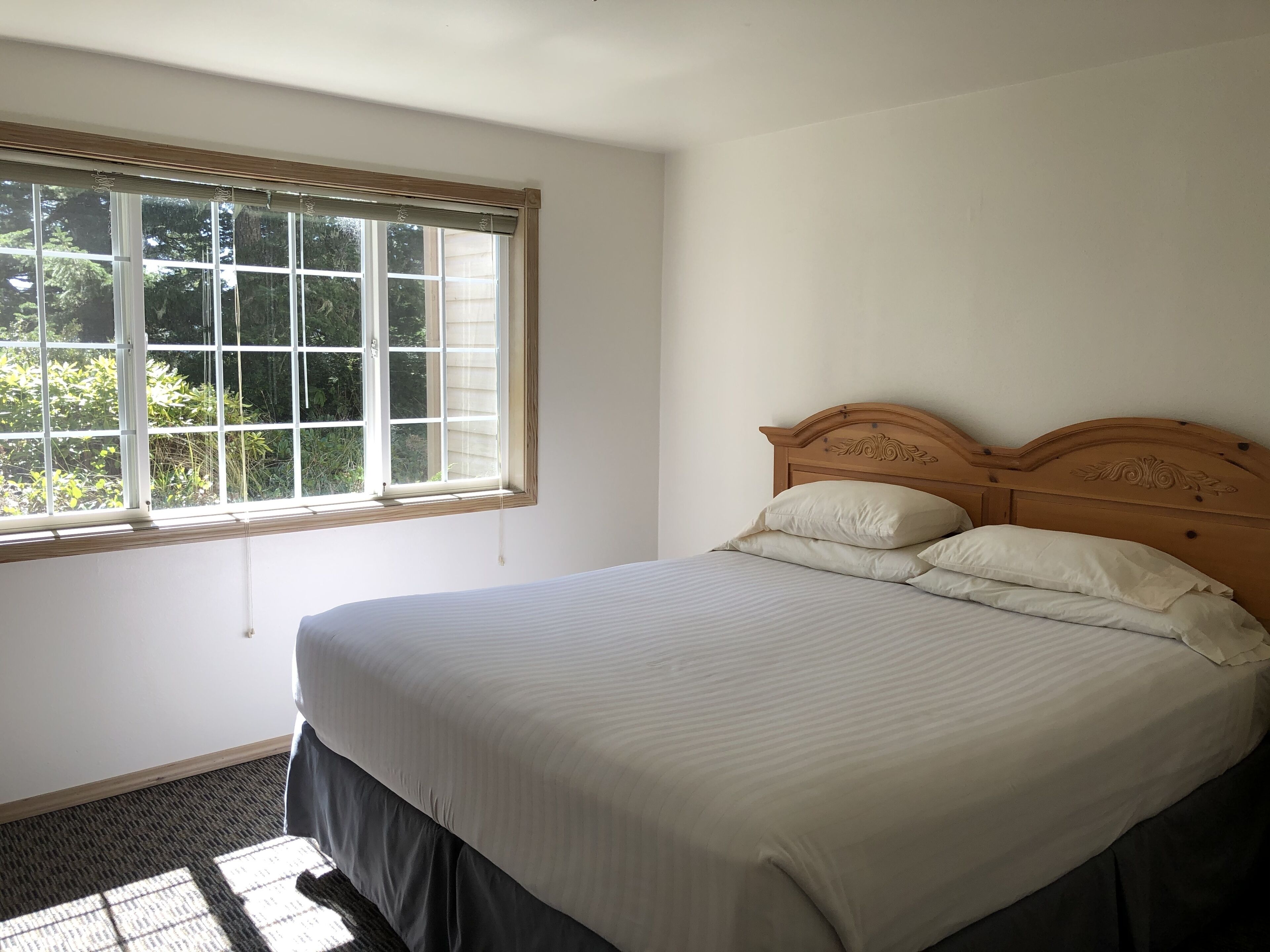Ein Schlafzimmer mit großem Fenster, einem Holzkopfteil und einem ordentlich bezogenen Bett.