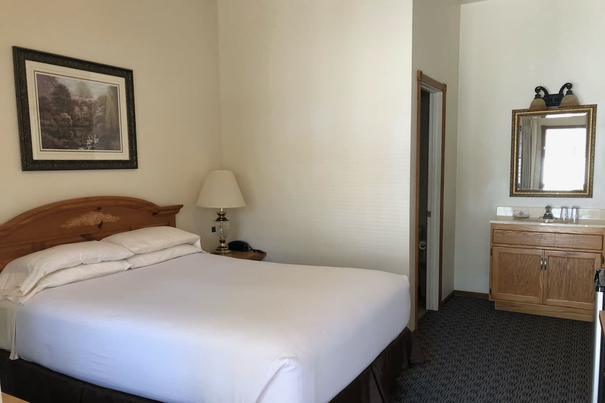A hotel room with a large bed, a bedside table with a lamp, a wooden dresser, and a framed picture on the wall.