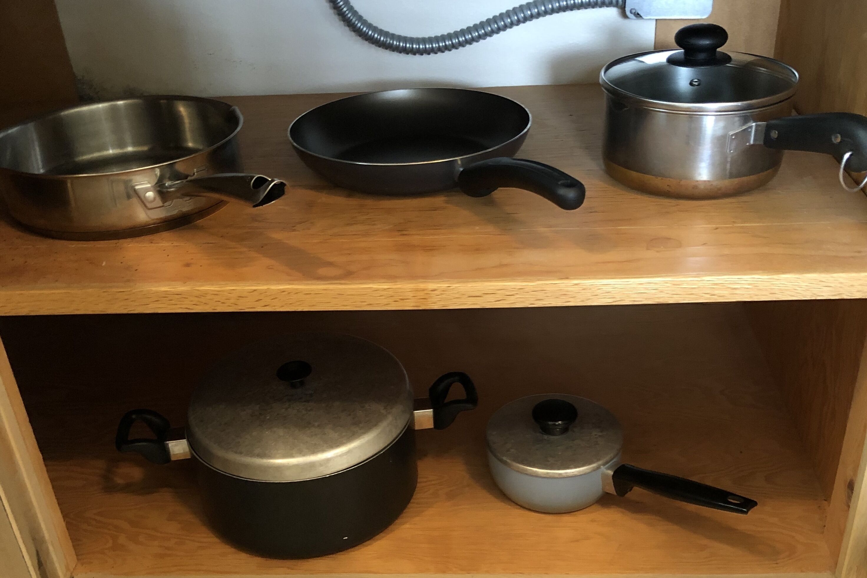 A kitchen shelf with various cookware items including pots, pans, and a frying pan.