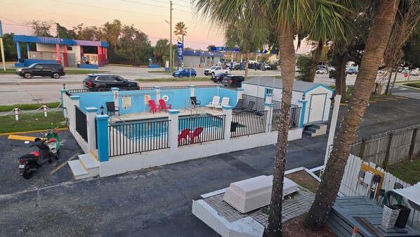 Un área de piscina amurallada con piscina, sillas de descanso y una zona de estar cubierta.