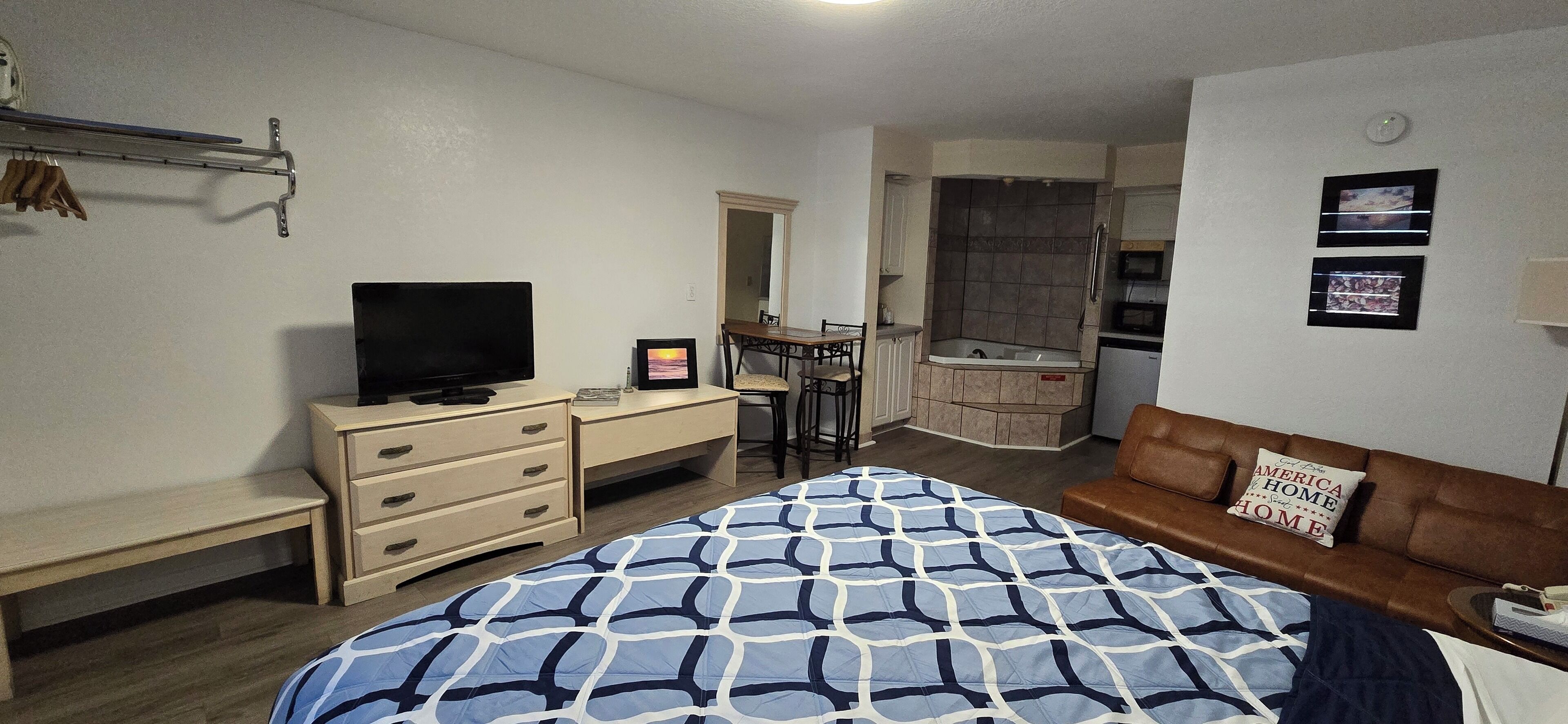 Een slaapkamer met een bed, een televisie, een bureau, een stoel, een bruine leren bank en een kleine badkamer met douche en wastafel.