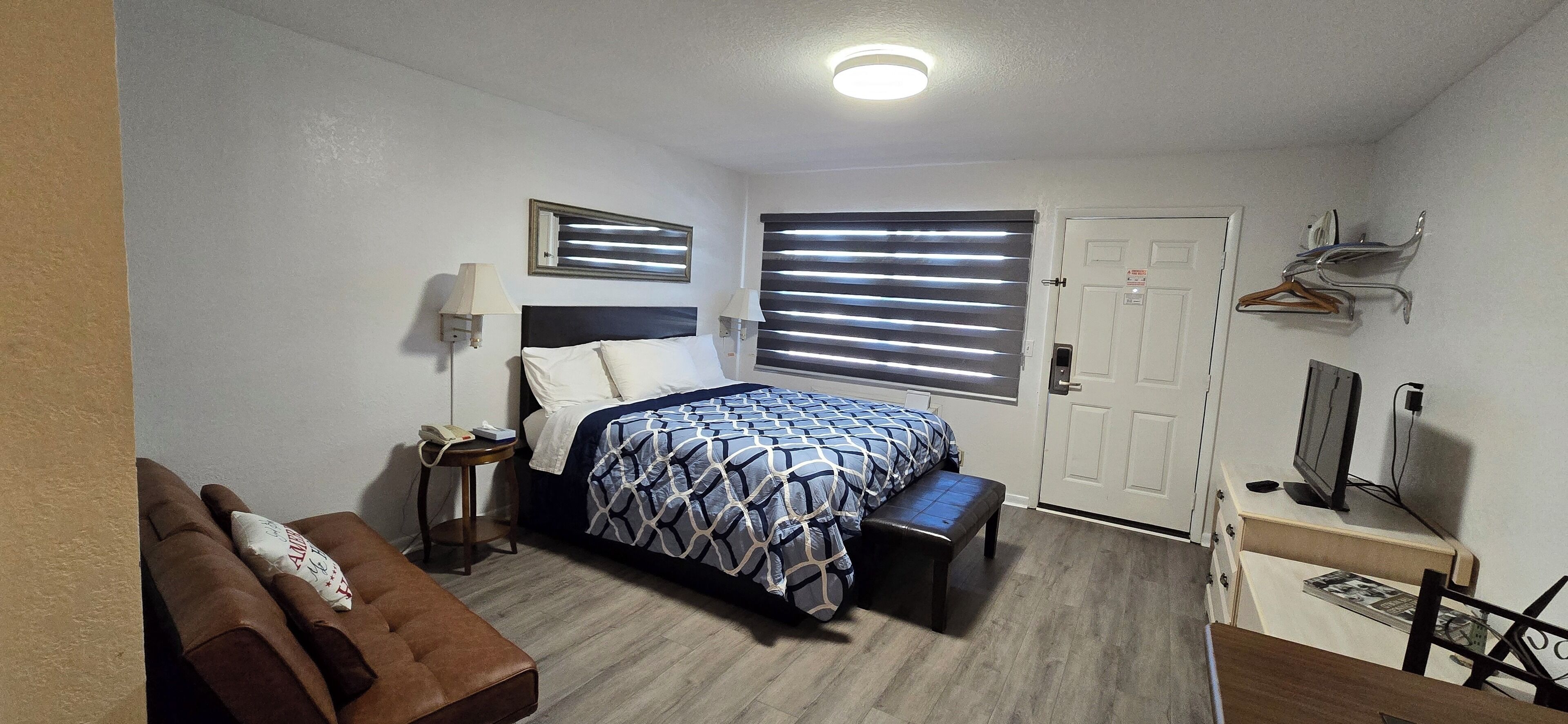 Une chambre d’hôtel comprenant un lit, des tables de chevet, un banc, une télévision, un porte-manteau et une porte.