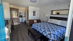 A hotel room with a bed, a desk with a chair, a small kitchenette, a brown sofa, and a bench. - Merida Inn and Suites (St. Augustine)