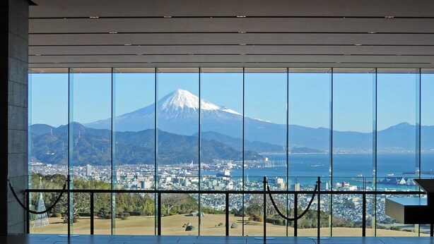Una habitación con grandes ventanales que ofrecen vistas a un paisaje urbano y una montaña.