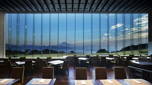Un restaurante con amplios ventanales que ofrecen vistas a un paisaje montañoso. Las mesas están dispuestas con salvamanteles y cubiertos.