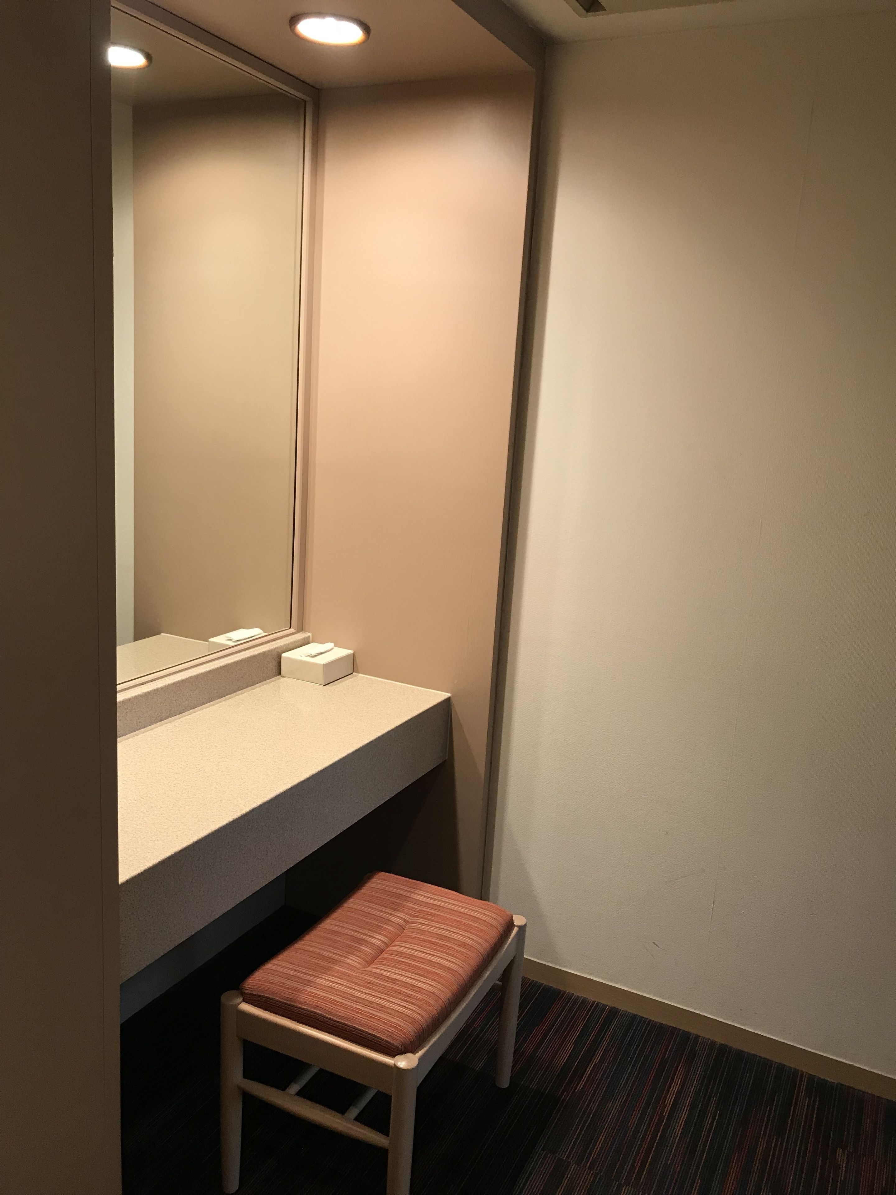 A small, private bathroom with a sink, mirror, and a chair.