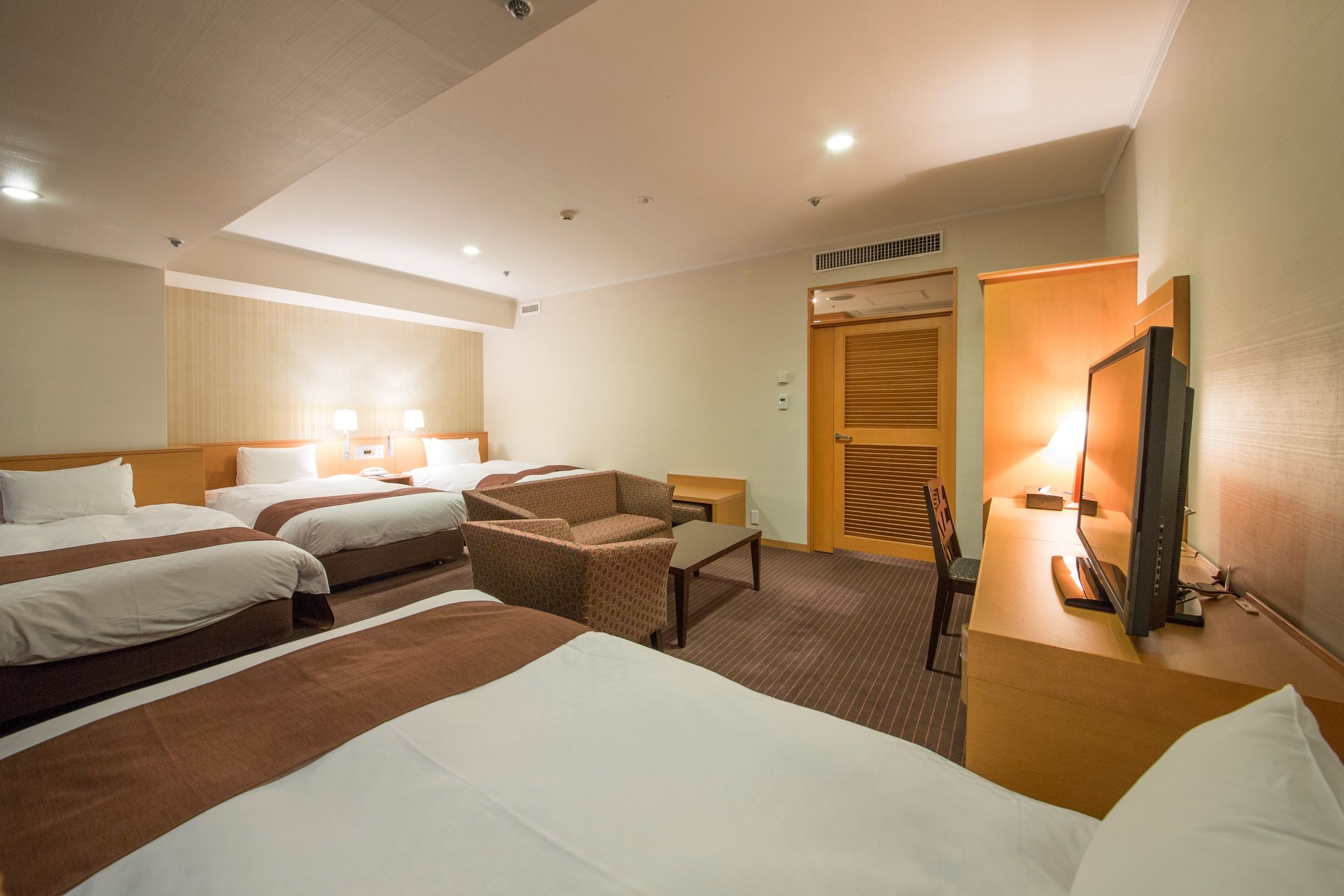Habitación de hotel con tres camas, un escritorio, una silla y un televisor.