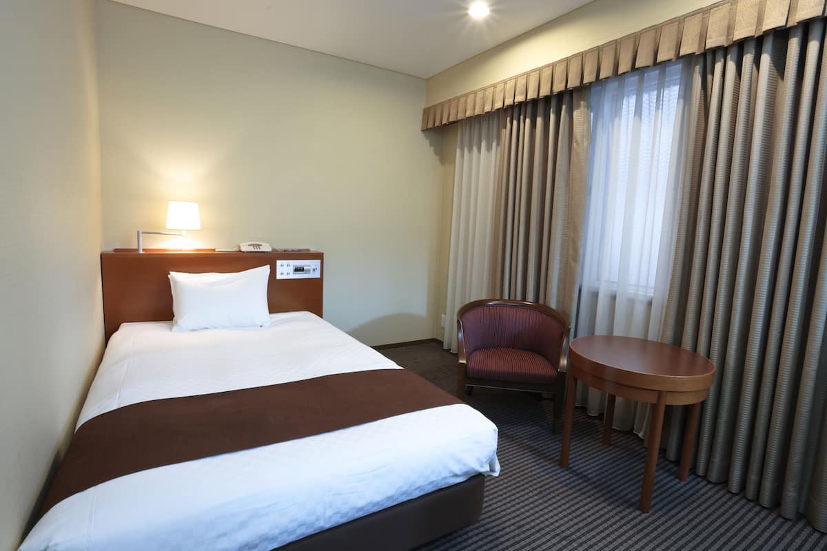 A hotel room with a large bed, a bedside table with a lamp, a chair, and a small table.