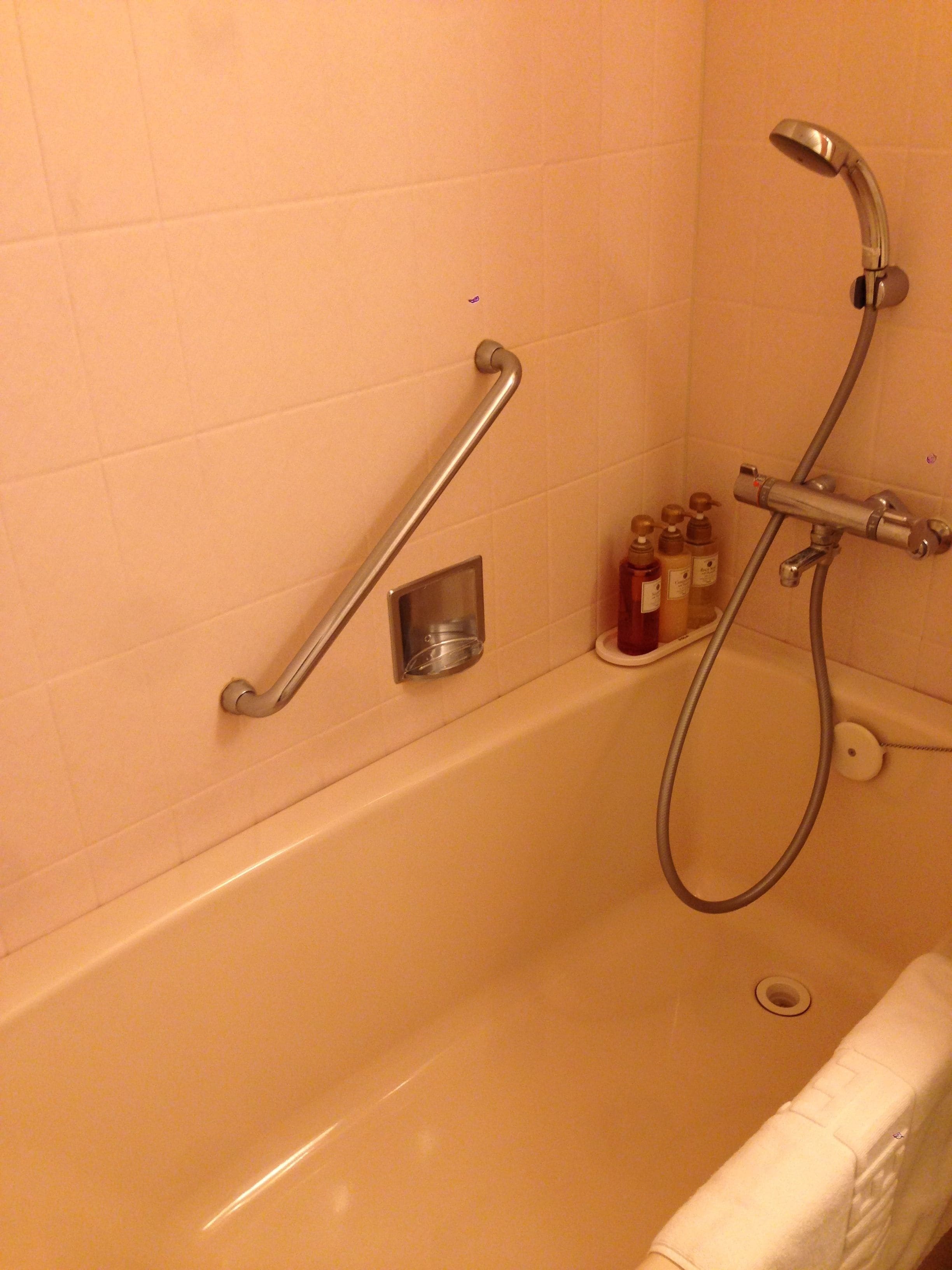 A bathroom with a bathtub, a shower, and a handrail. There are bottles of toiletries on the wall.