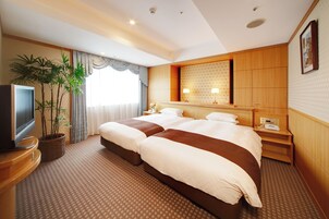 Habitación de hotel con una cama grande, televisor, planta y ventana con cortinas.
