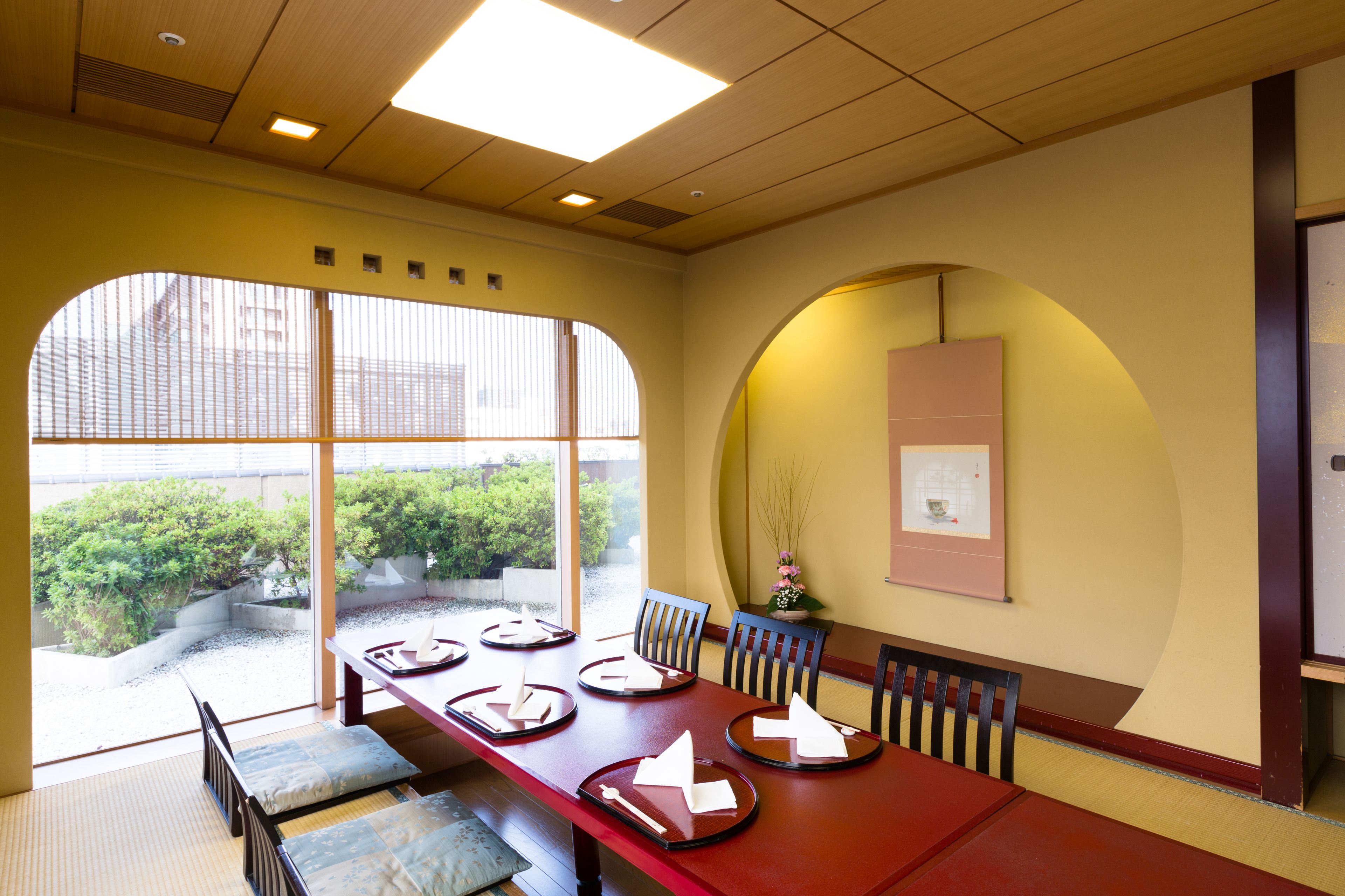 A dining area with a long table, chairs, and a view of greenery outside.