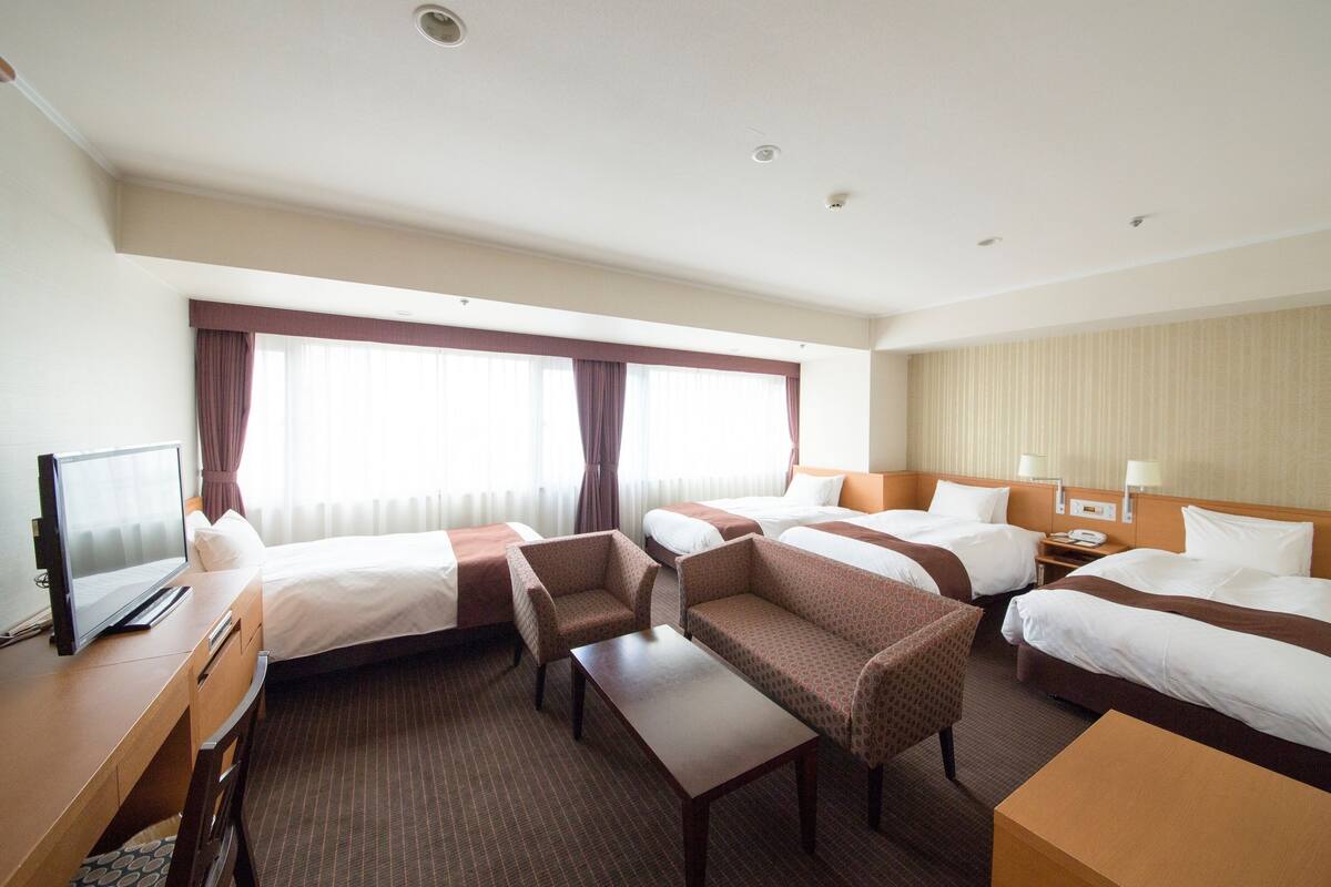 A hotel room with two beds, a desk with a computer, a chair, and a small table.