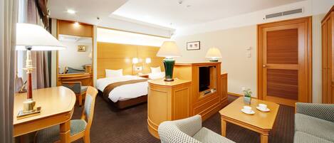 A hotel room with a bed, a desk with a lamp, a TV, and a seating area with chairs.