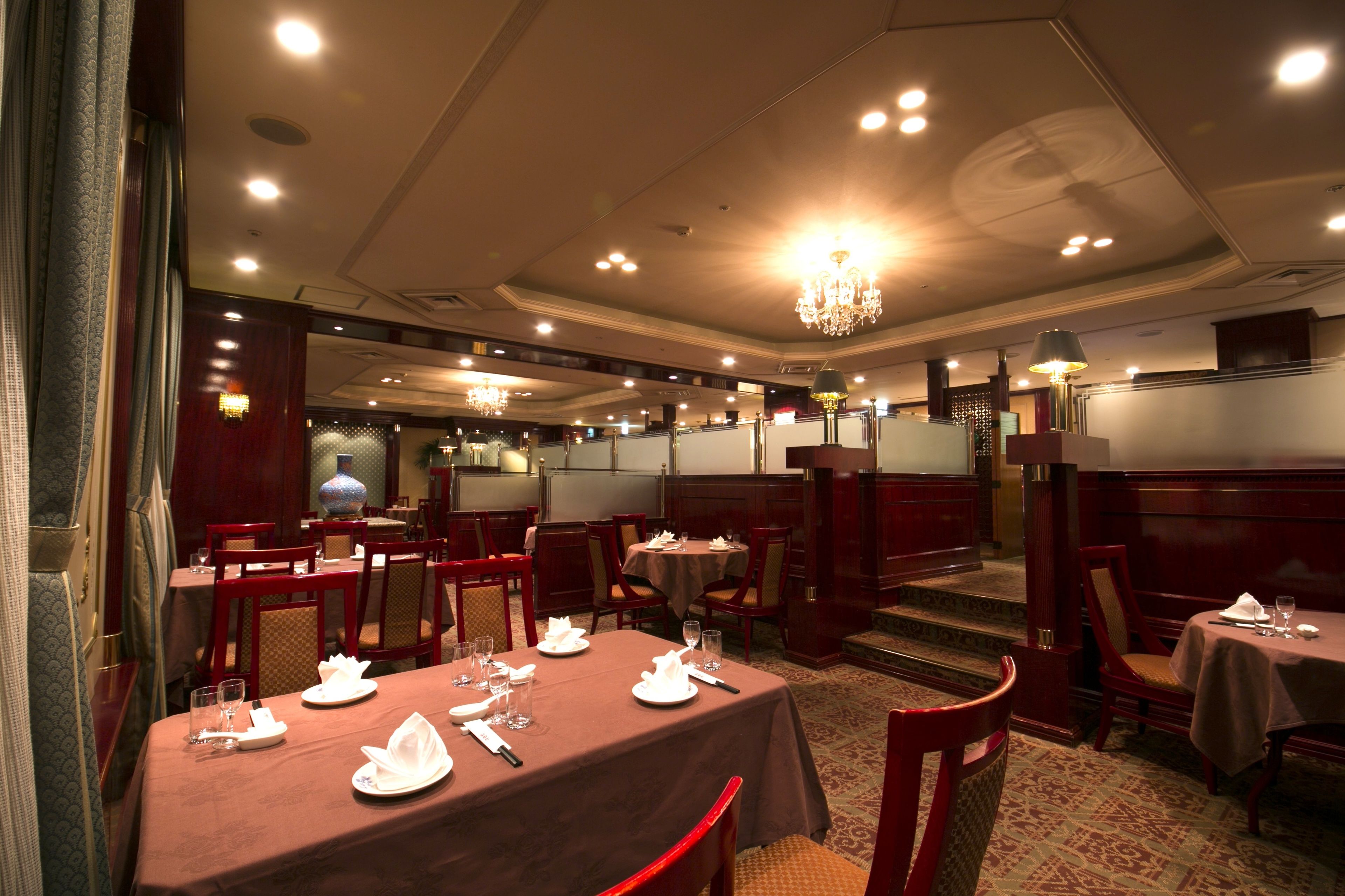 A restaurant with multiple tables set for dining, featuring a classic interior design with wooden furniture and chandeliers.