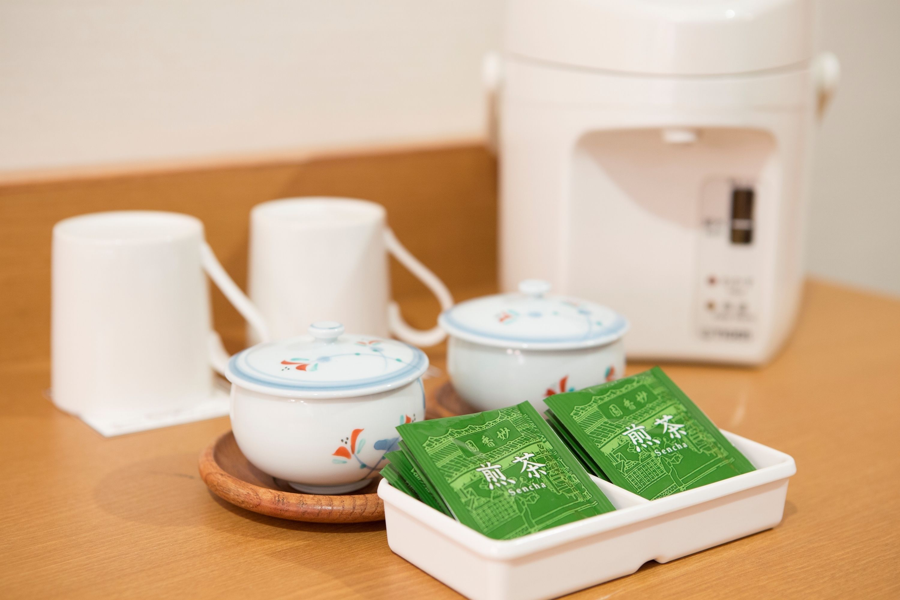 A tea set with two teapots, two cups, and a green tea packet on a wooden tray.