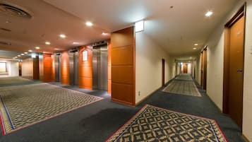 Ein Hotelgang mit Teppichböden, Holztüren und zwei Aufzügen.