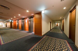 A hotel hallway with carpeted floors, wooden doors, and two elevators.