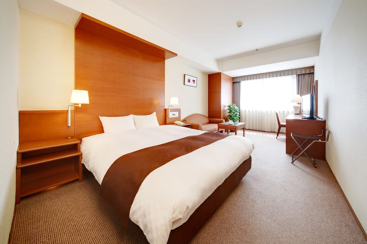 A hotel room with a large bed, a desk, a chair, a lamp, and a window with curtains.