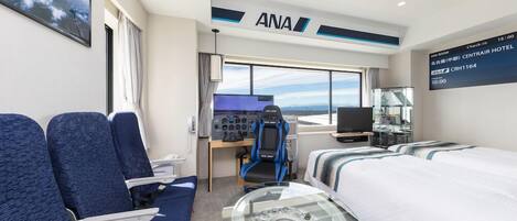 A modern hotel room with a large window, a desk with a computer, a bed, and a seating area with blue upholstered chairs.