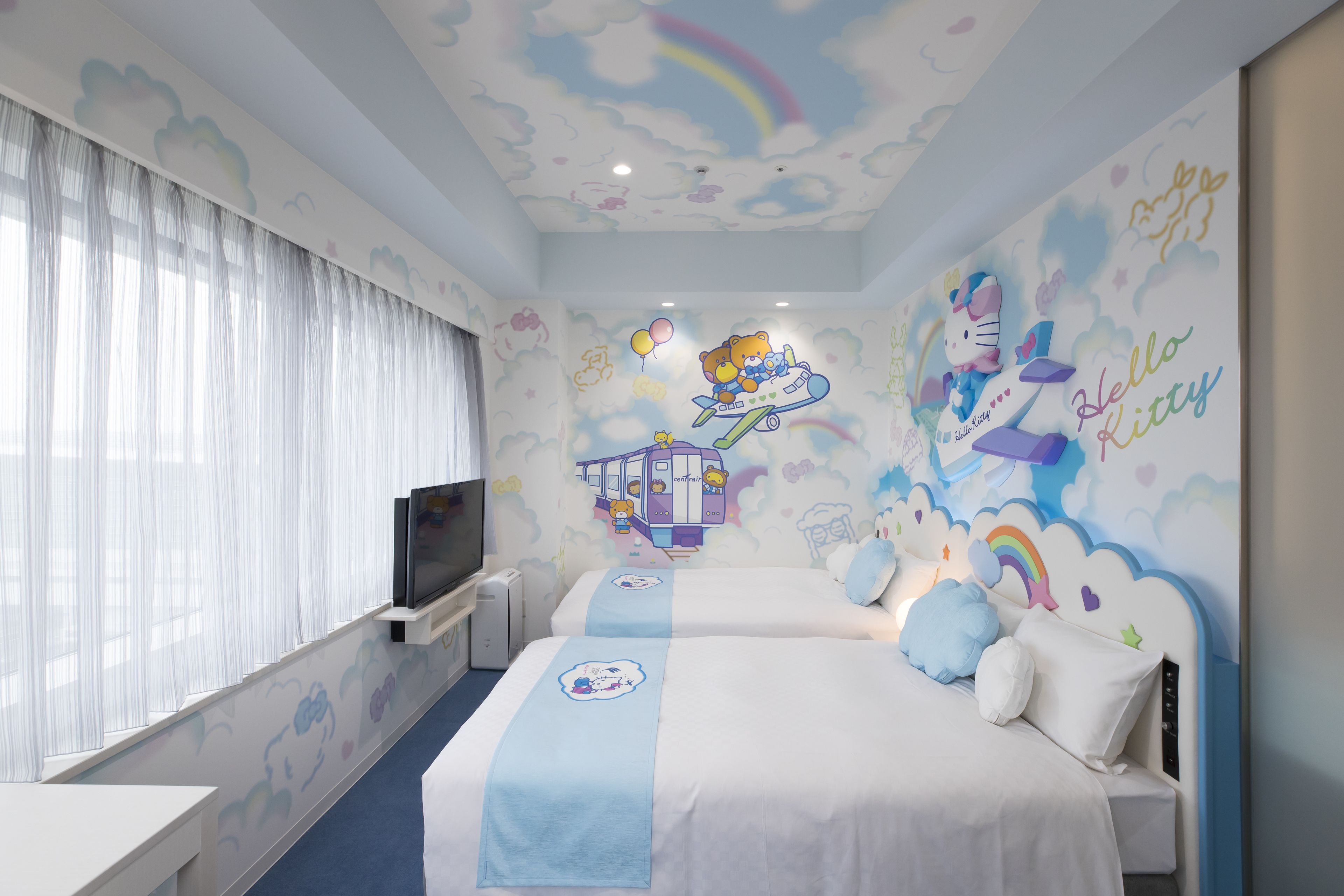 A children's room with two beds, a TV, and a mural with Hello Kitty and Hello Kitty's dog.