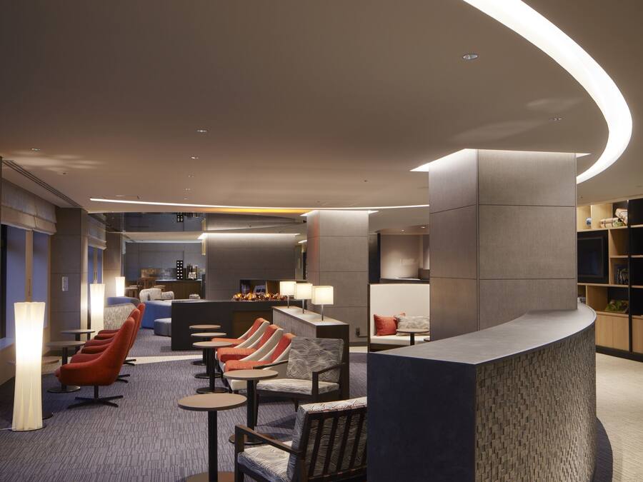 A modern hotel lobby with a curved reception desk, comfortable seating areas, and a bar.