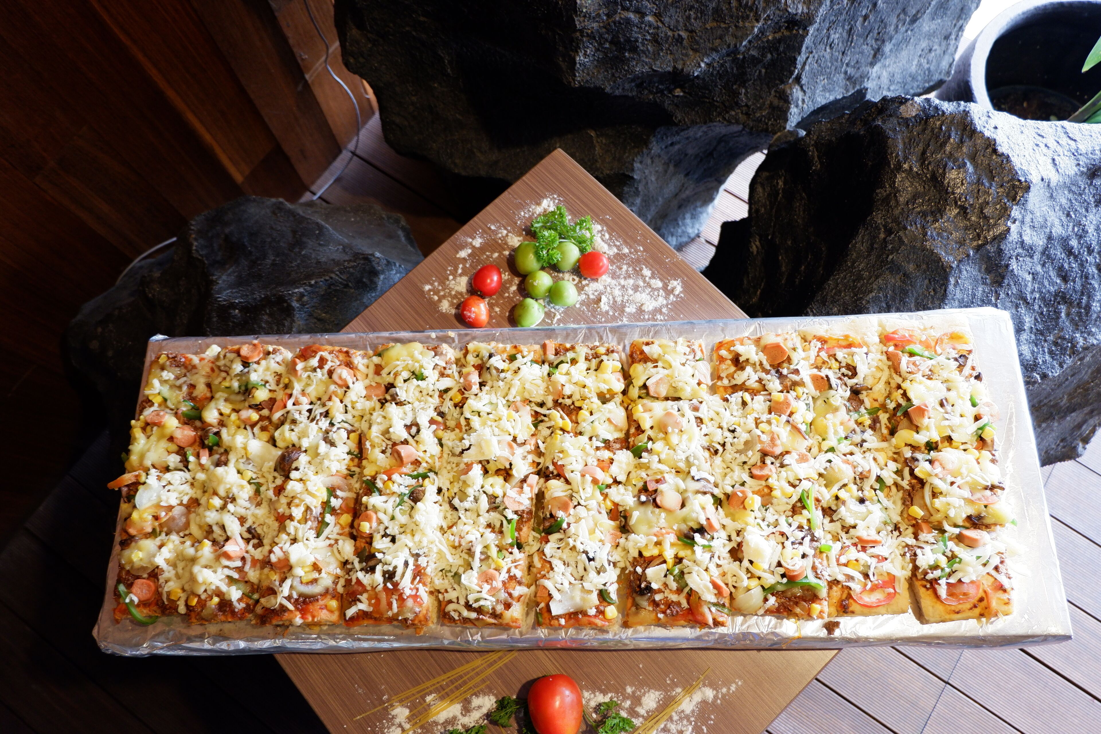 A large rectangular pizza with various toppings, placed on a wooden table with a rustic background.
