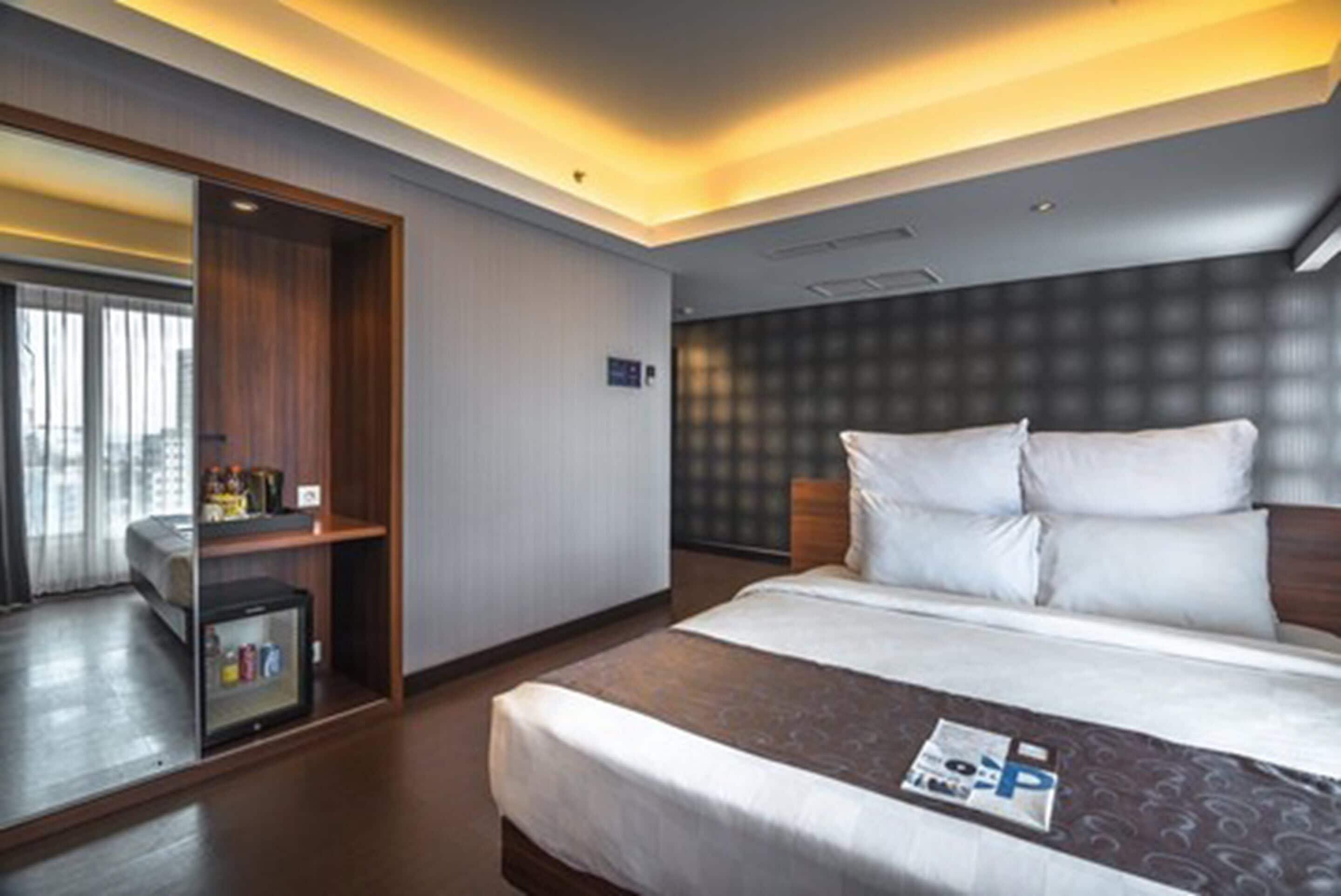 A hotel room with a bed, a small bedside table, a wardrobe, and a window with curtains.