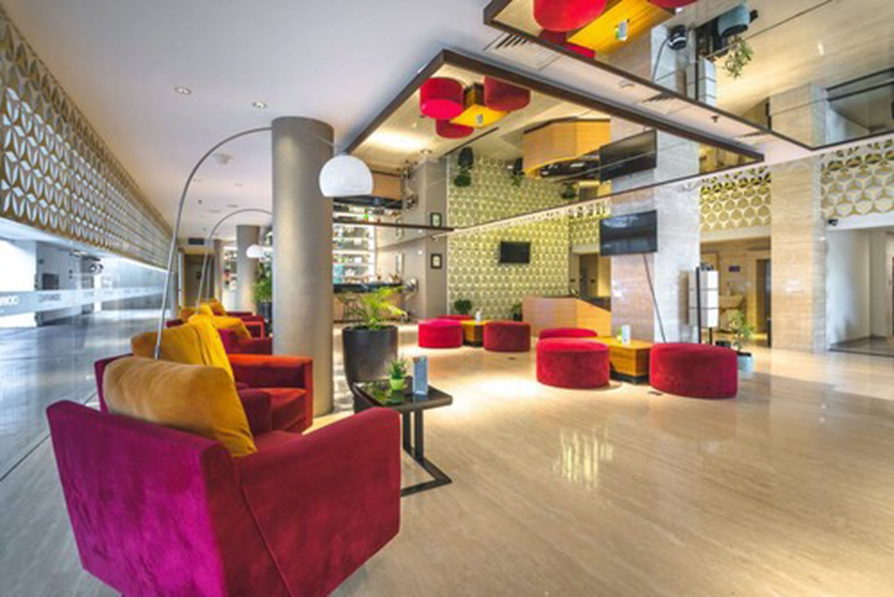 A spacious lobby with red and yellow seating, a central plant, and a patterned wall.