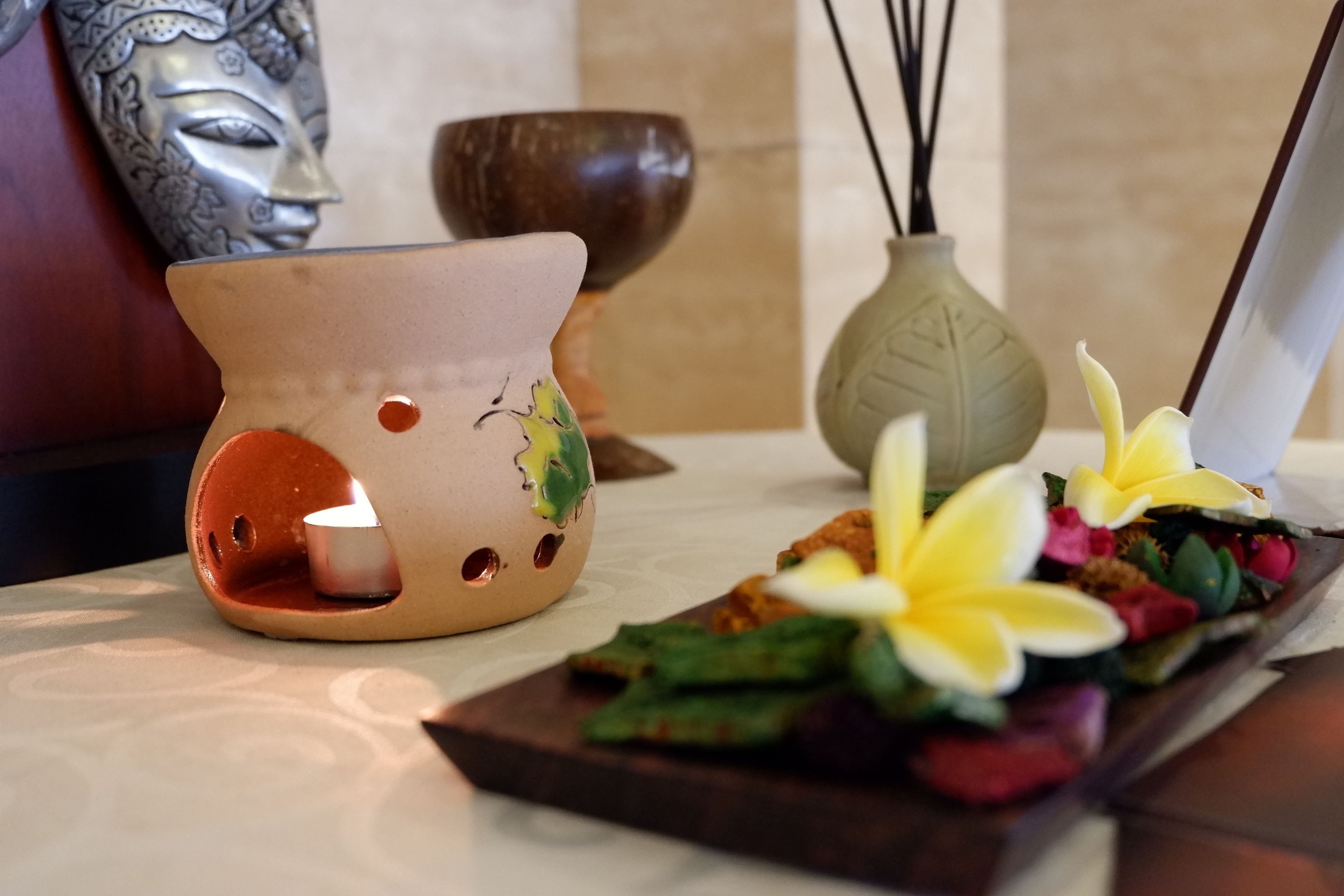 A candle holder with a lit candle, a decorative mask, and a tray with flowers and snacks.