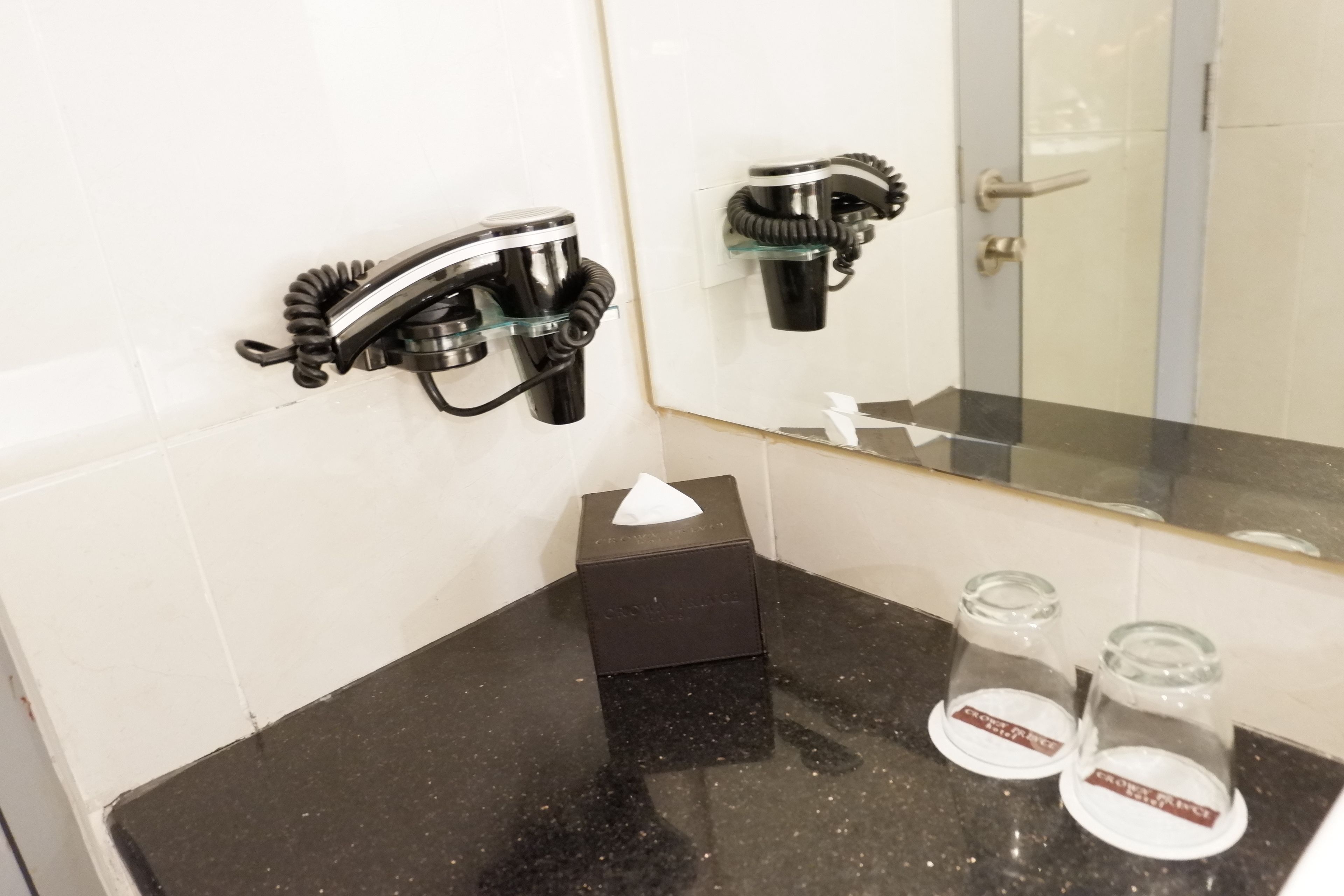 Un baño con encimera negra, dispensador de toallas, caja de pañuelos y dos recipientes de vidrio sobre el lavamanos.