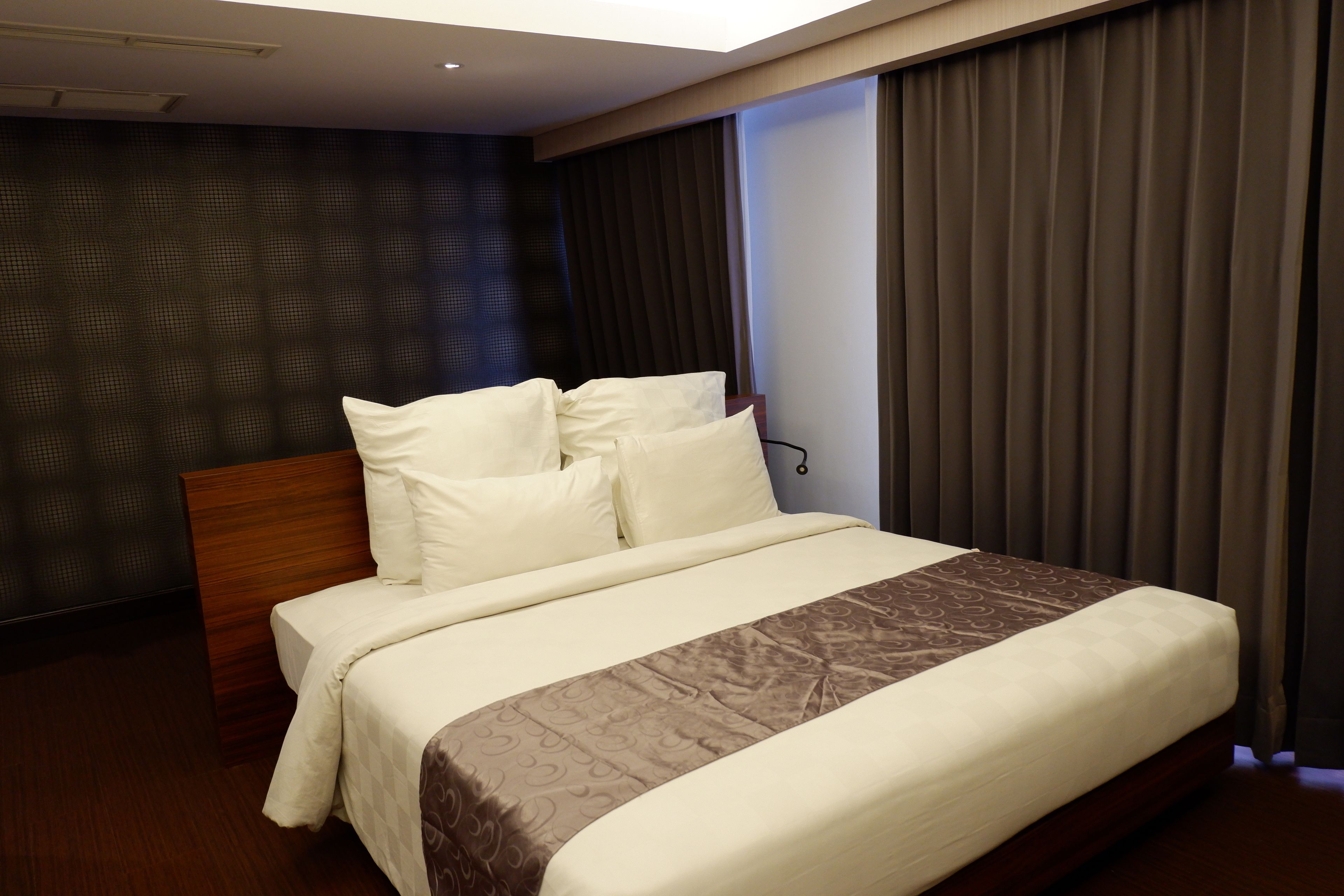 A hotel room with a large bed, dark patterned wall, and a window with curtains.