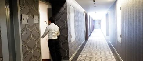 A hotel corridor with patterned walls and carpet, a man at an elevator, and doors marked with years.