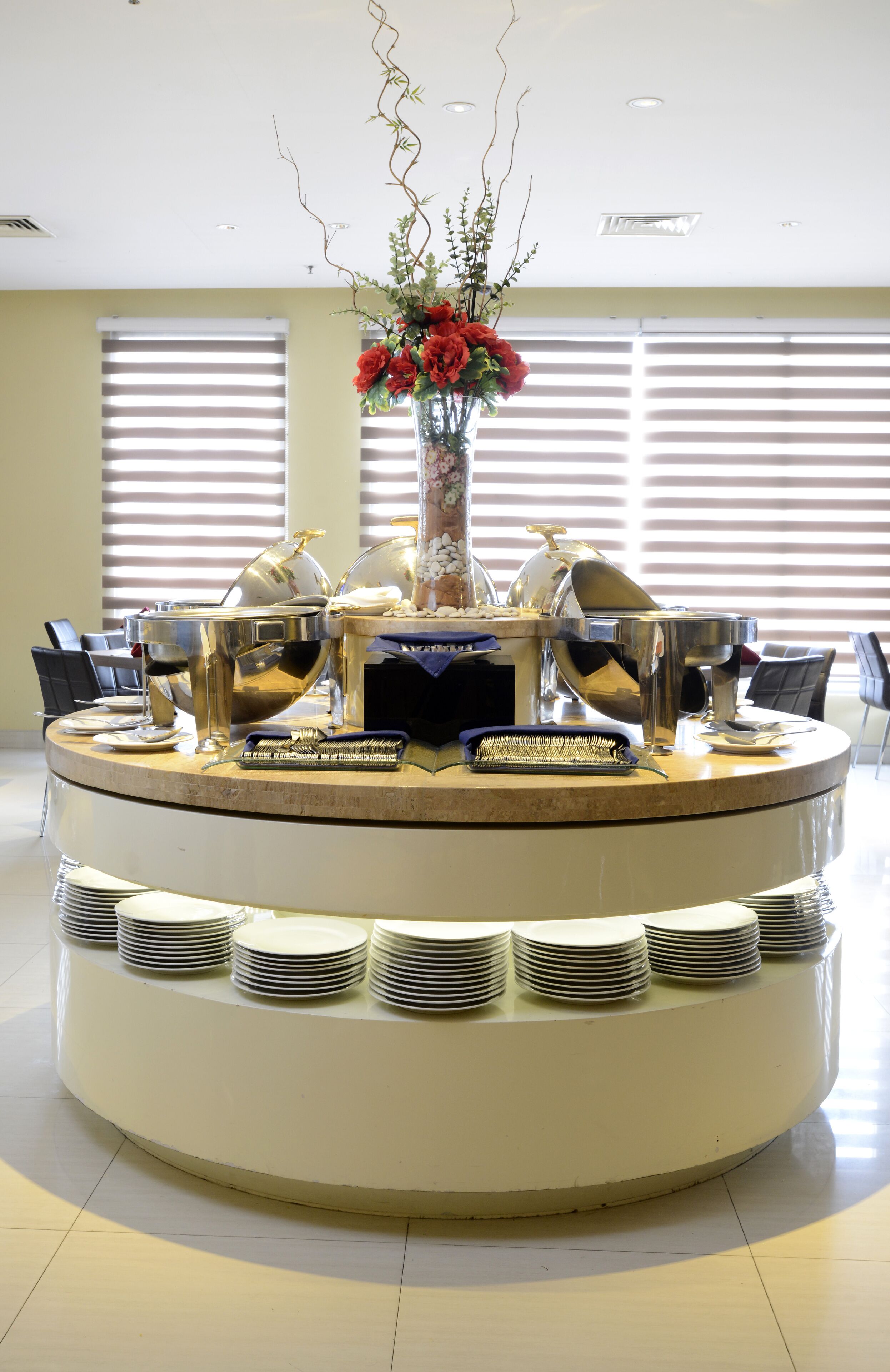A buffet setup with multiple serving stations, a central floral arrangement, and a stack of plates.