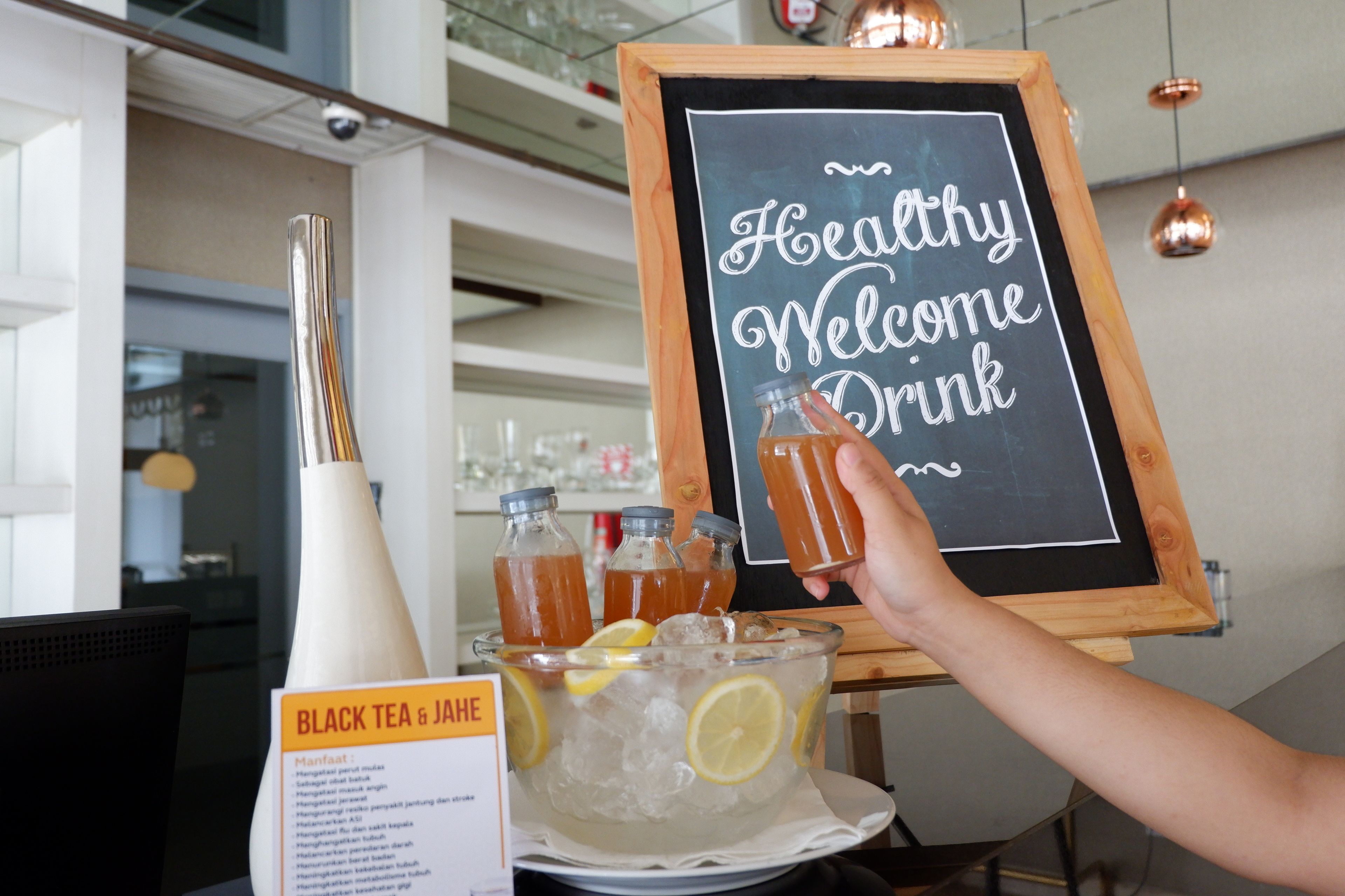 A person holding a drink in front of a sign that reads "Healthy Welcome Drink."