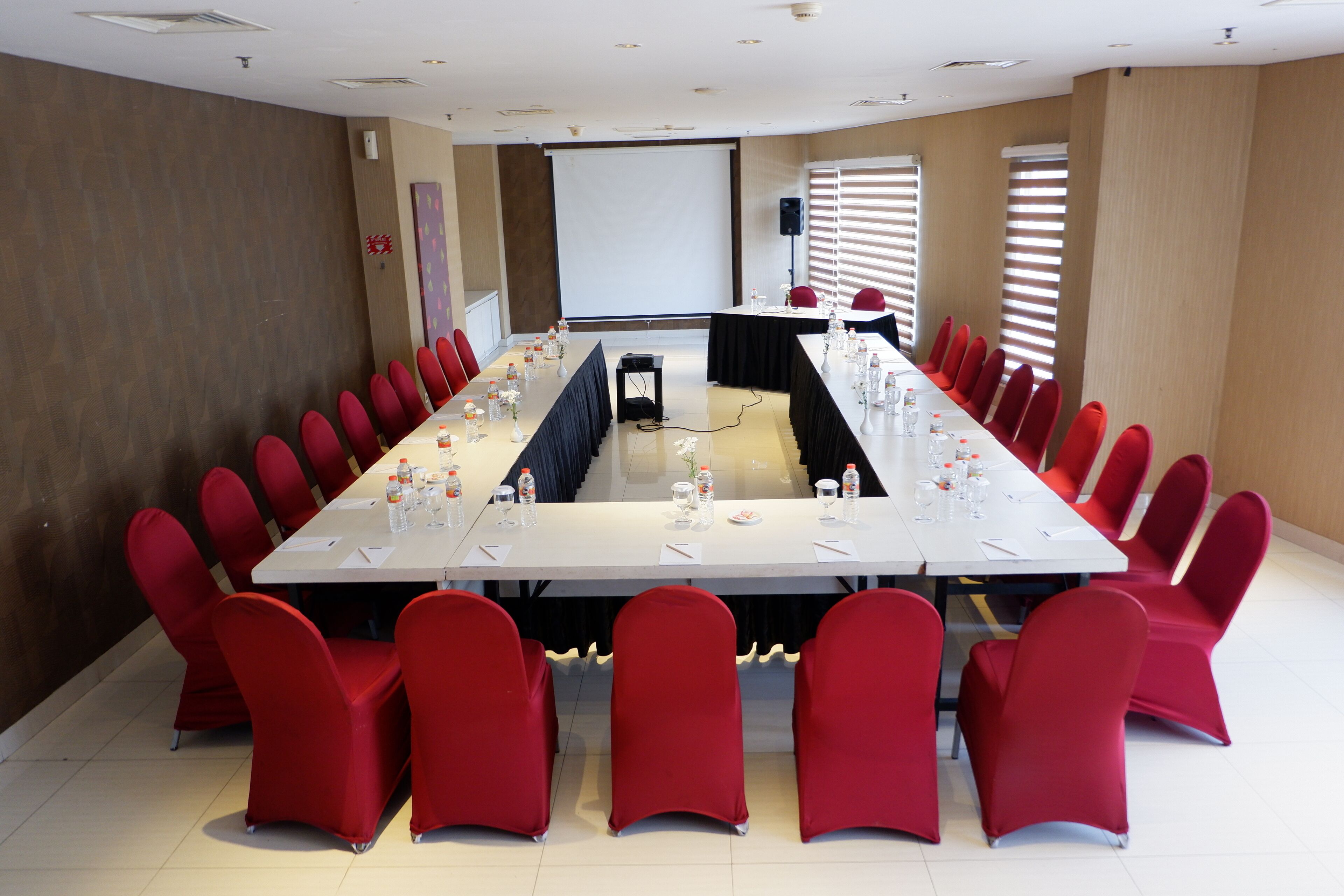 A conference room with a long table, red chairs, and a projector screen.