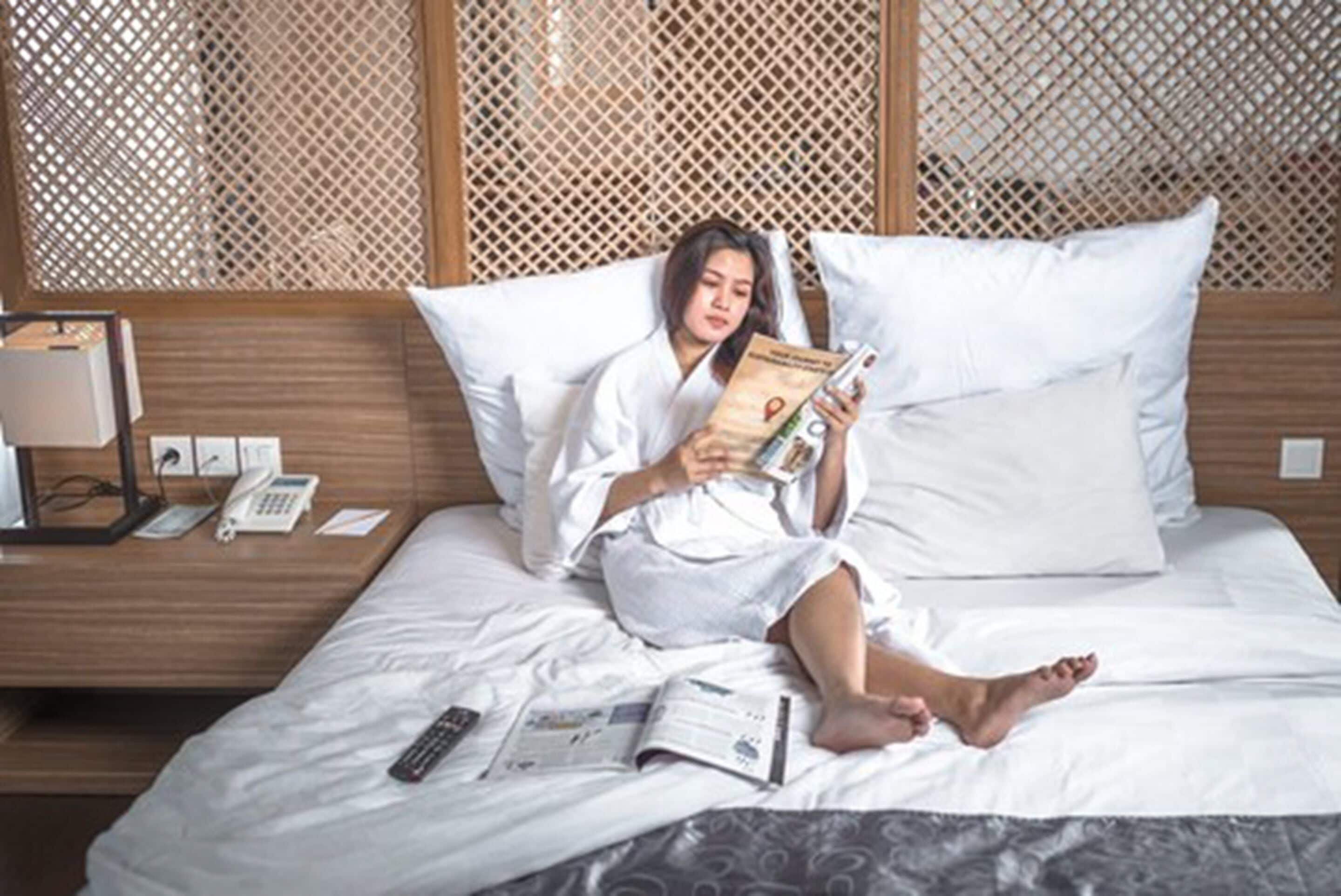 Hotelkamer met een bed, nachtkastje met telefoon en lamp, en een raam met een traliewerk.