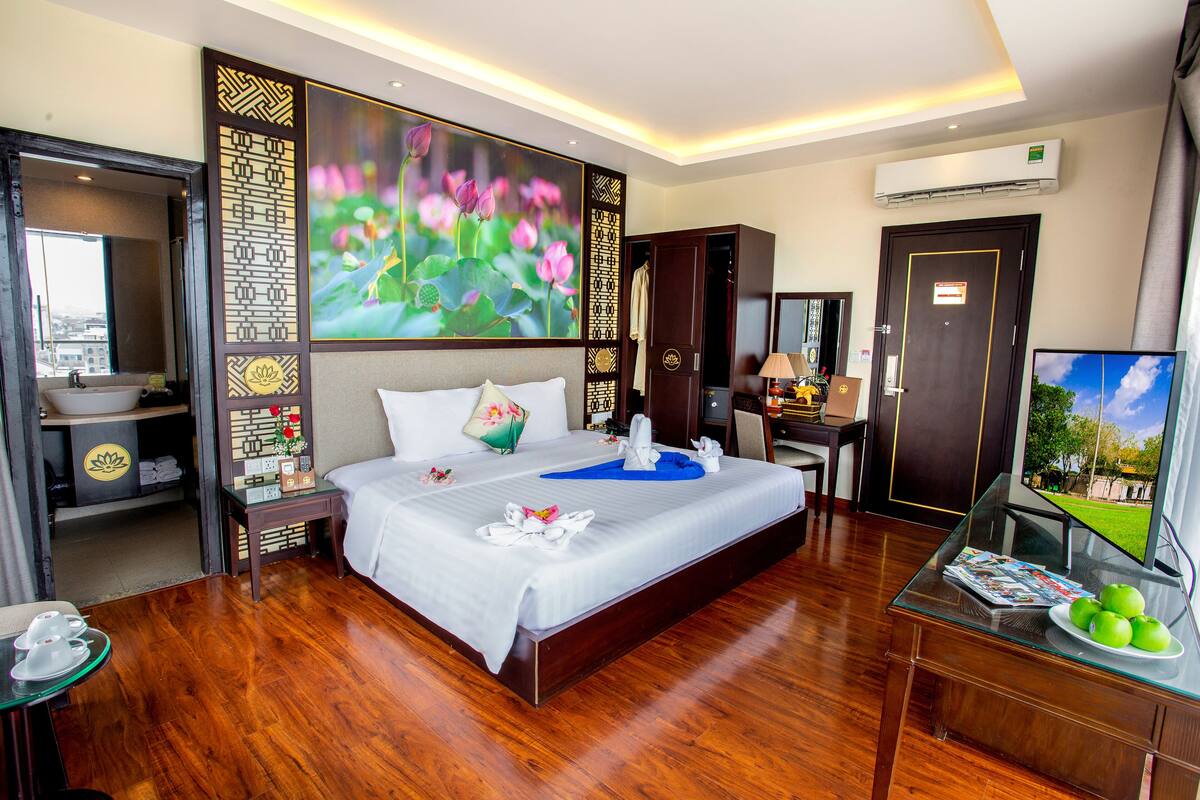 Une chambre d’hôtel avec un grand lit, une télévision, un bureau avec un ordinateur et une salle de bain visible à travers une porte ouverte.