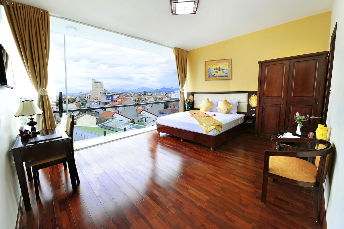 Une chambre d’hôtel avec un grand lit, un plancher en bois, une vue sur la ville et un balcon.